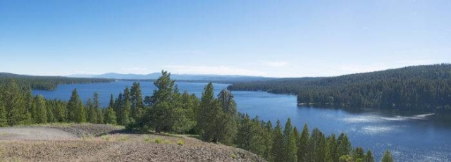 A crystal blue lake, forested hills, and a cloud-spotted blue sky.