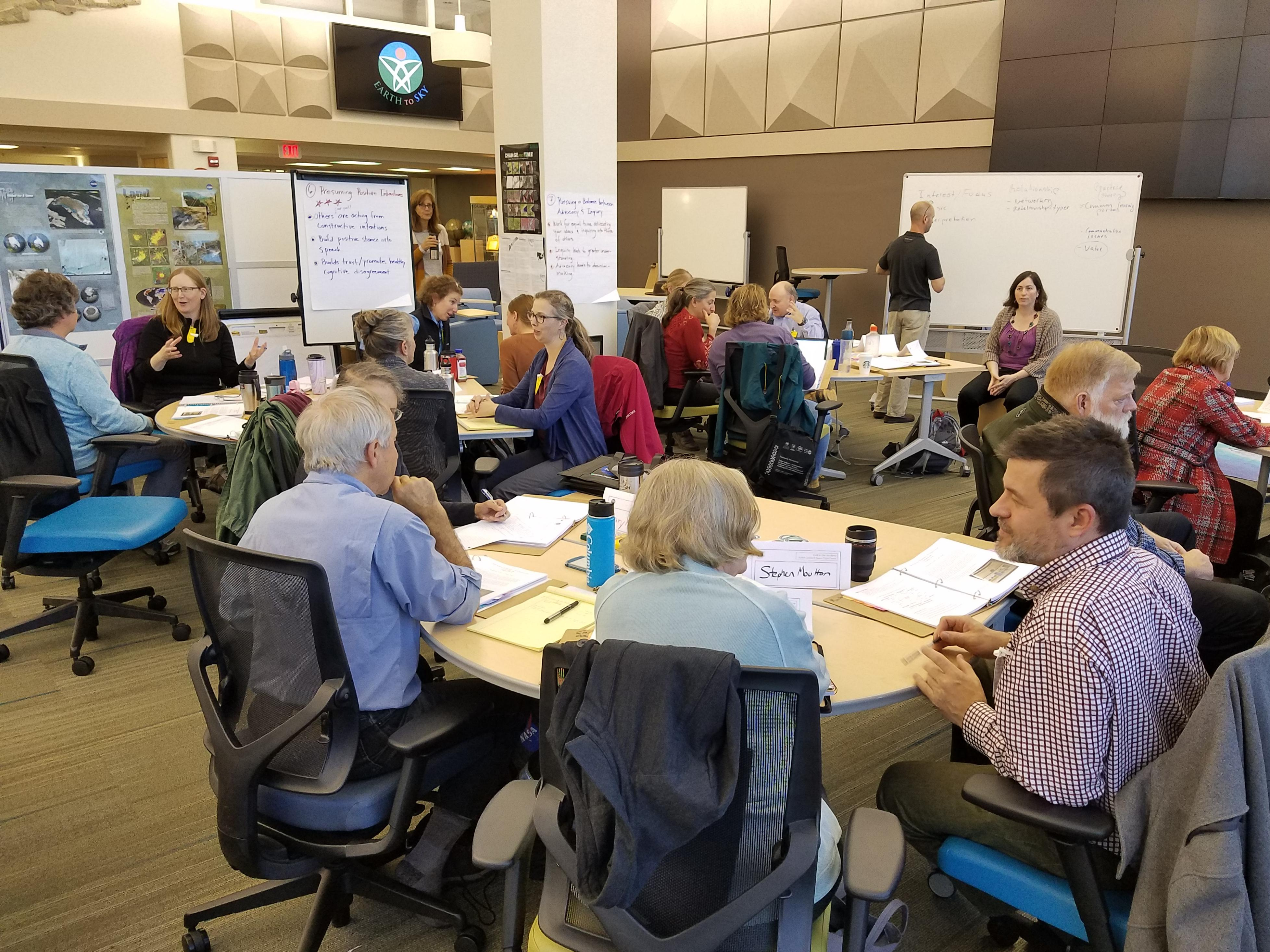 Groups of people work together at circular tables in a large, open room