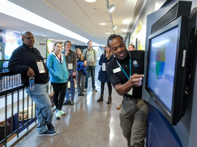 Group watches a presenter pointing at chart on screen.